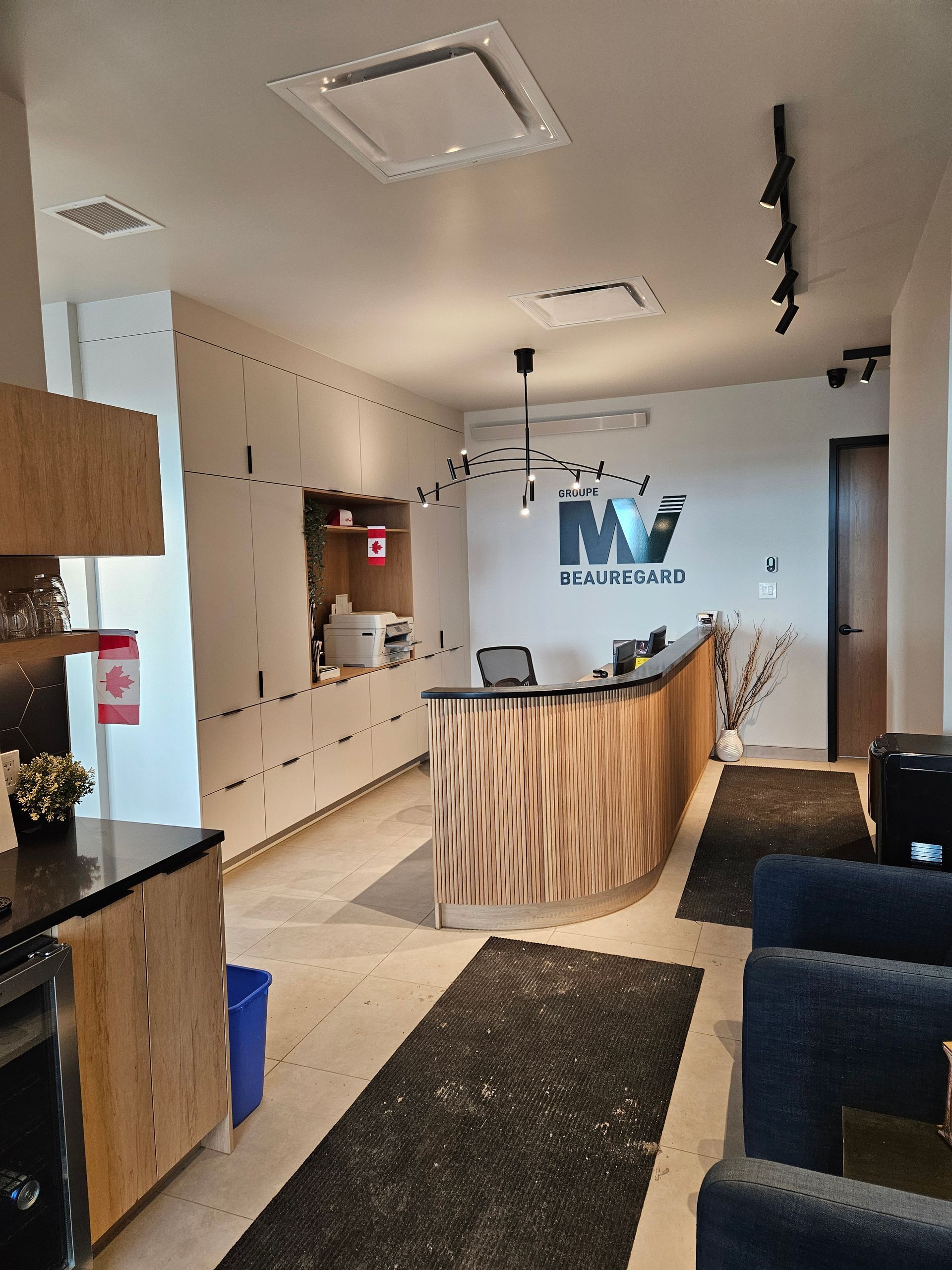 Un espace d'accueil lumineux avec un bureau incurvé en bois veiné, le logo de l'entreprise sur le mur du fond et des chaises bleues.