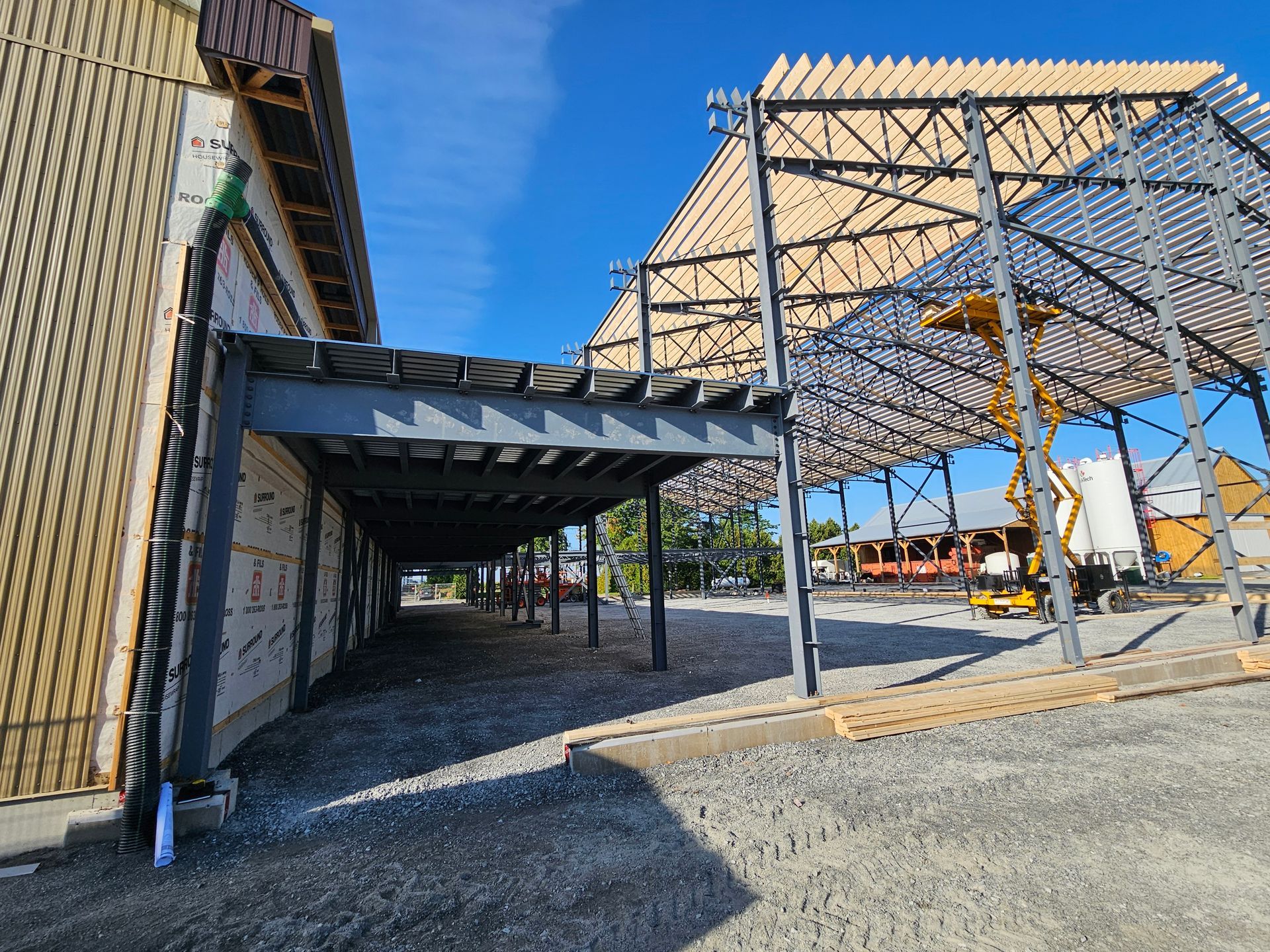 Un chantier de construction montrant la structure d'un nouveau bâtiment sous un ciel bleu éclatant, avec une nacelle élévatrice jaune en arrière-plan.