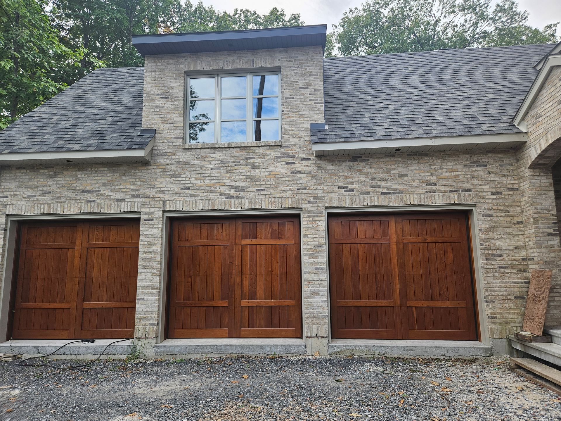 Un bâtiment en pierre avec trois portes de garage en bois et une lucarne au-dessus, se détachant sur un fond d'arbres.