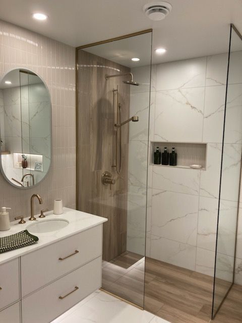 Une salle de bains moderne avec un meuble-lavabo blanc, un miroir rond et une douche à l'italienne revêtue de carrelage imitation bois et en marbre blanc.