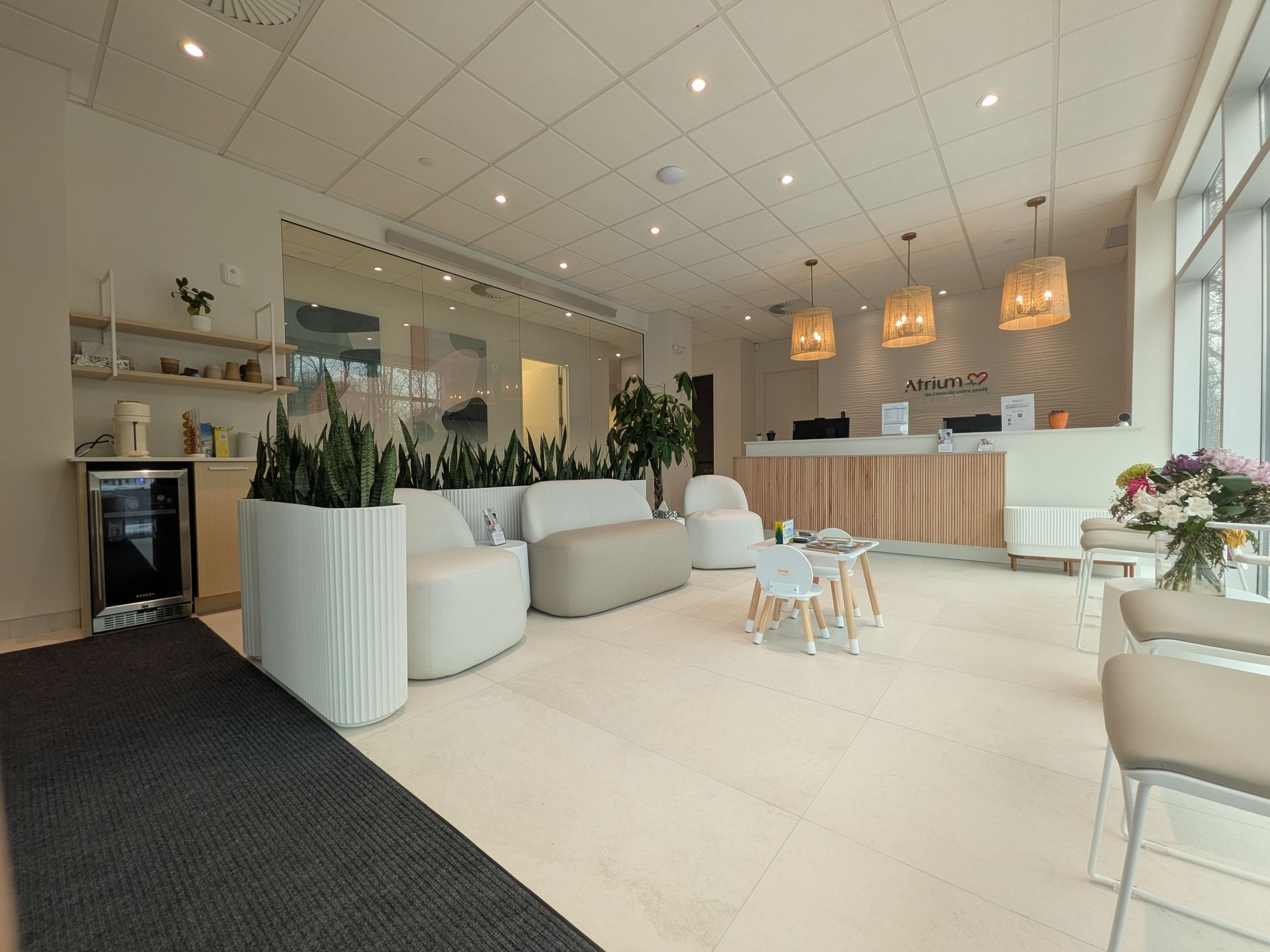 Un hall d'entrée lumineux et moderne avec des sièges aux tons clairs, des plantes en pot, une réception et une petite table pour enfants.