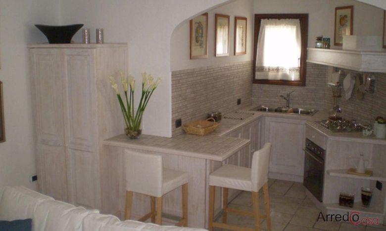 Cucina moderna bianca con isola, pensili, lavello, finestra e sgabelli da bar in legno.