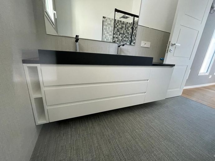 Mobile bagno moderno bianco con piano, lavabo e specchio neri in una stanza luminosa.