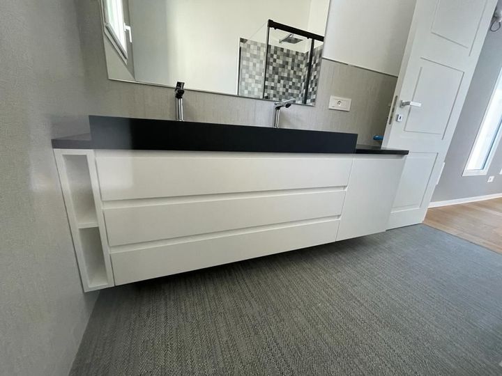 Mobile bagno moderno bianco con piano, lavabo e specchio neri in una stanza luminosa.