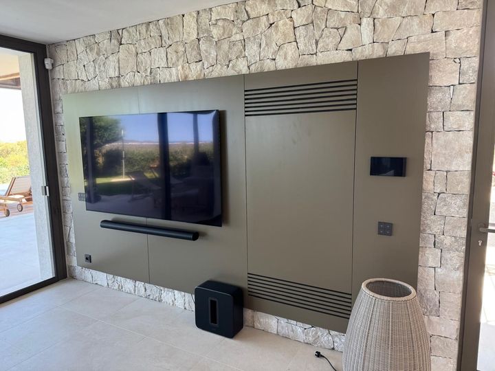 Parete da patio moderna con TV a schermo piatto montata a parete, rivestimento in pietra e lanterna decorativa sul pavimento.