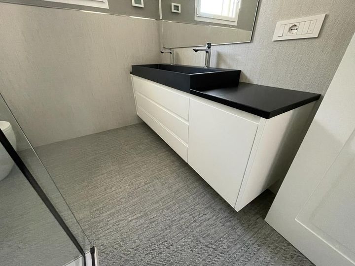 Mobile bagno bianco con piano e lavabo neri in una stanza piastrellata di grigio.