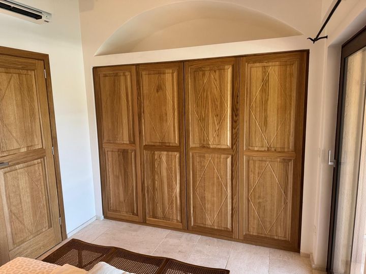 Camera da letto con armadi a muro con ante in legno e una porta in legno sulla sinistra, sotto un soffitto a volta.