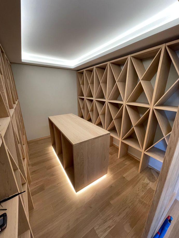 Stanza moderna in legno con scaffalature geometriche, un tavolo centrale e illuminazione a pavimento a LED dai toni caldi.