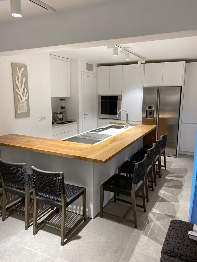 Cucina moderna con isola in legno, sgabelli neri, mobili bianchi ed elettrodomestici in acciaio inossidabile.