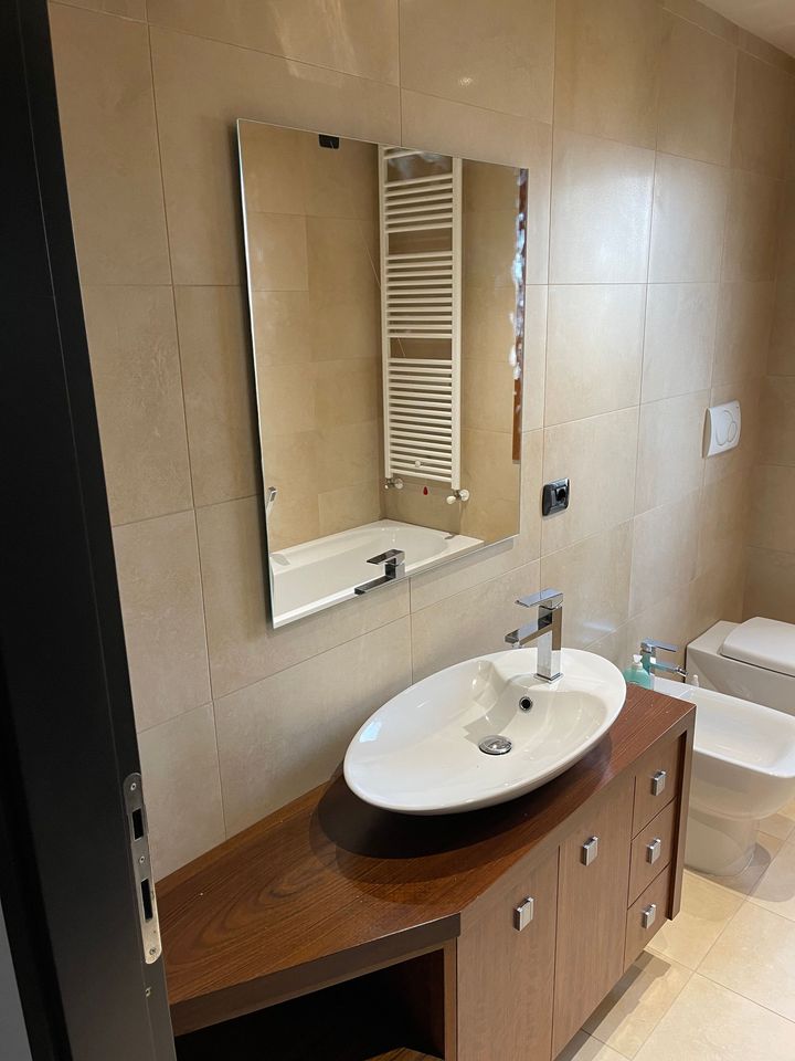 Mobile da bagno con lavabo ovale, specchio e parete piastrellata.