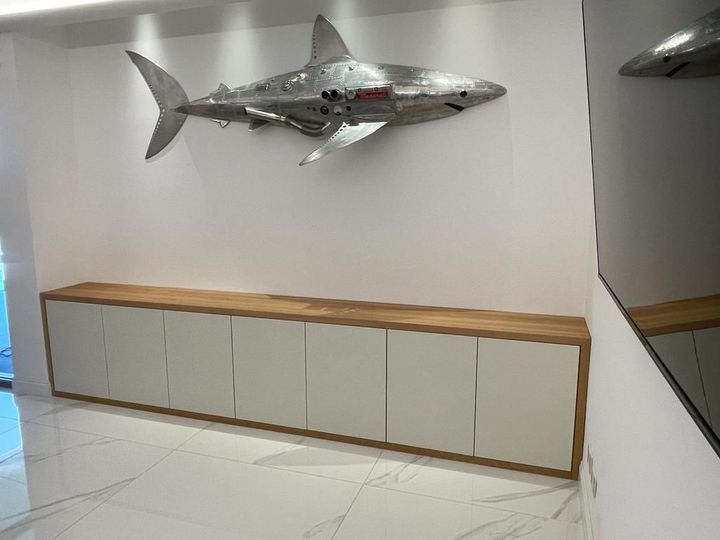 Scultura metallica a forma di squalo montata sopra un lungo armadio bianco in un corridoio moderno