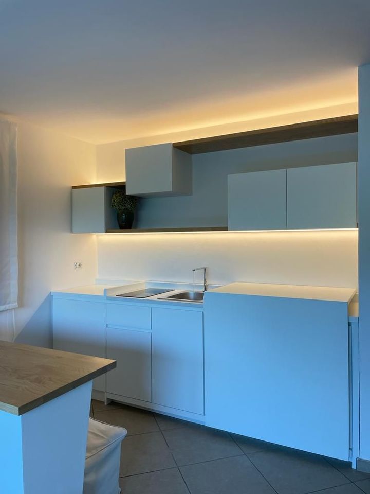 Cucina moderna bianca con illuminazione sottopensile blu e piano di lavoro grigio.
