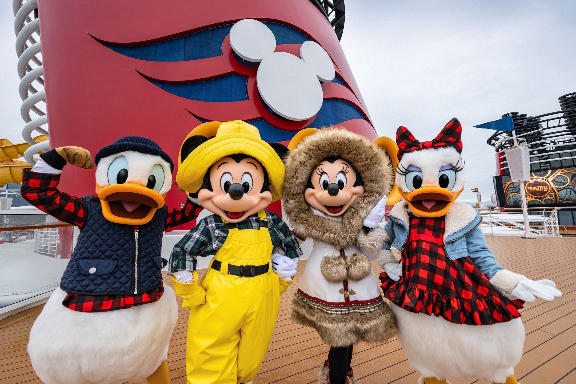 Donald, Mickey, Minnie, and Daisy Duck in winter outfits on a Disney cruise ship deck in front of a red funnel.