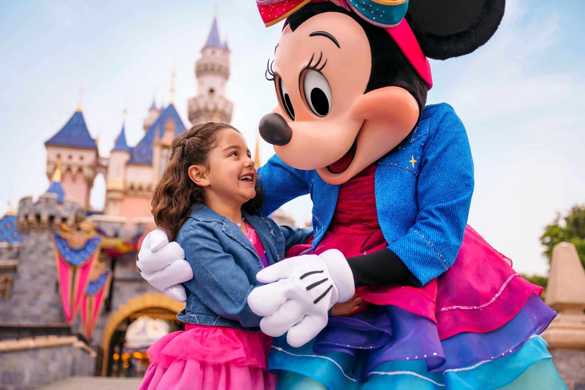 Girl hugging Minnie Mouse in front of a castle at a theme park, both smiling brightly