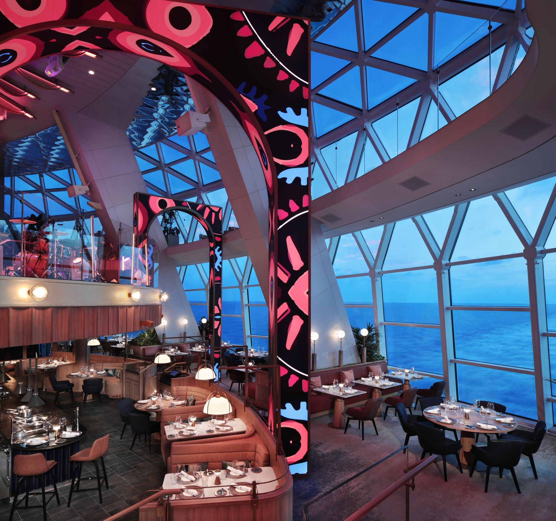 Modern seaside restaurant interior with pink-lit arches, glass walls, and tables overlooking the ocean at dusk