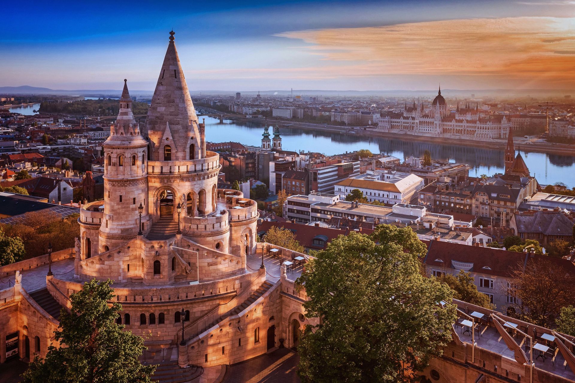 Sunset view of a cathedral overlooking a city and river, with warm orange sky and rooftops below