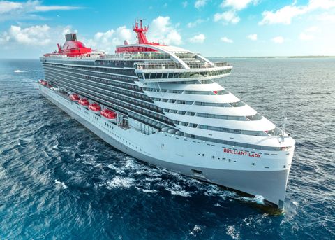 Large white cruise ship with red accents sailing on blue ocean under a partly cloudy sky