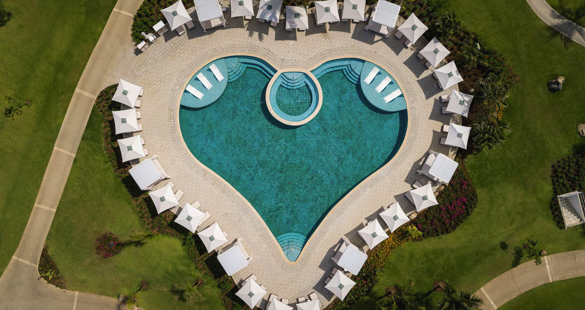 Heart-shaped swimming pool with turquoise water, white lounge chairs, and surrounding grass paths.