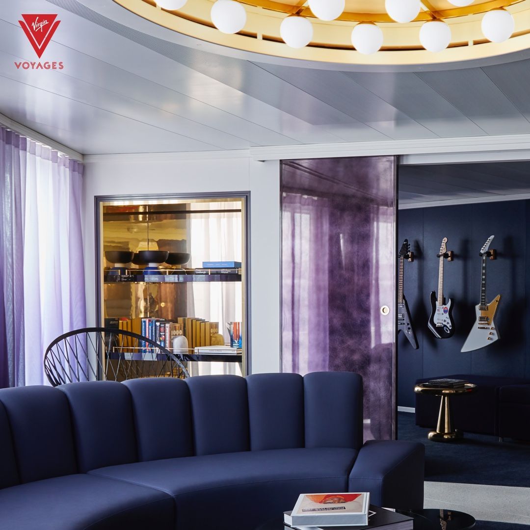 Modern living room with a curved navy sofa, purple curtains, display shelves, and guitars on a dark wall