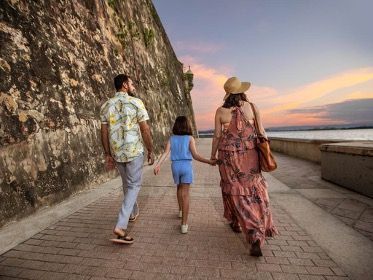 A family walks along a stone-walled path by the water at sunset.