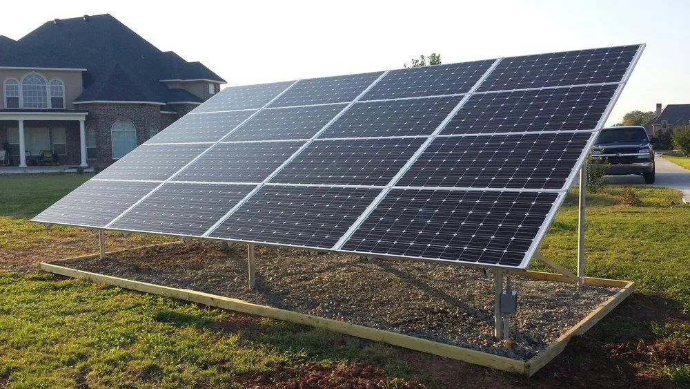 Solar panels mounted on a metal frame in a grassy field beside a house