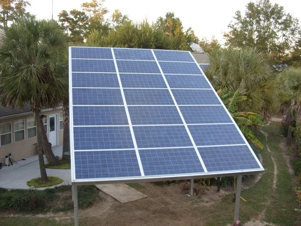 Solar panel array in a backyard, angled toward the sky. Green trees and a house are in the background.