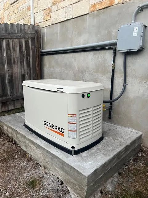 Outdoor backup generator on a concrete pad beside a house, connected to a gray wall-mounted electrical box.