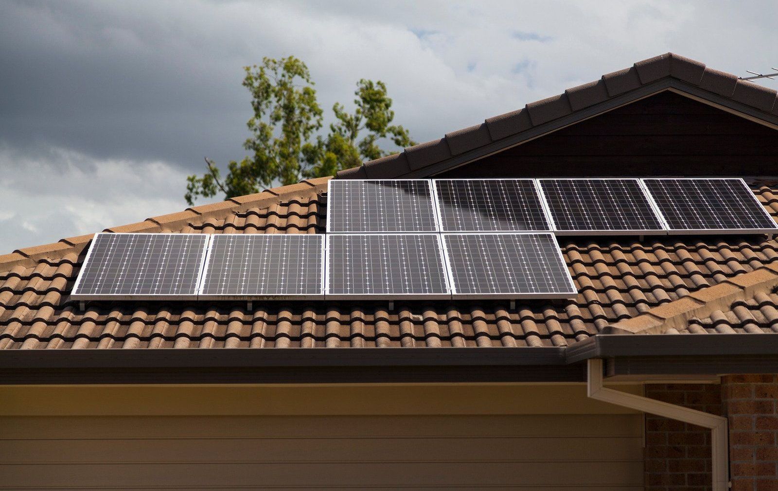 Solar panels installed on a brown tiled roof against a cloudy sky.