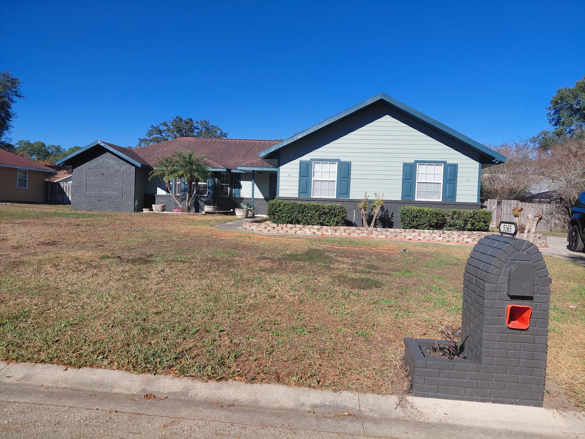 Single-story suburban house with a front lawn and a brick mailbox under a clear blue sky.