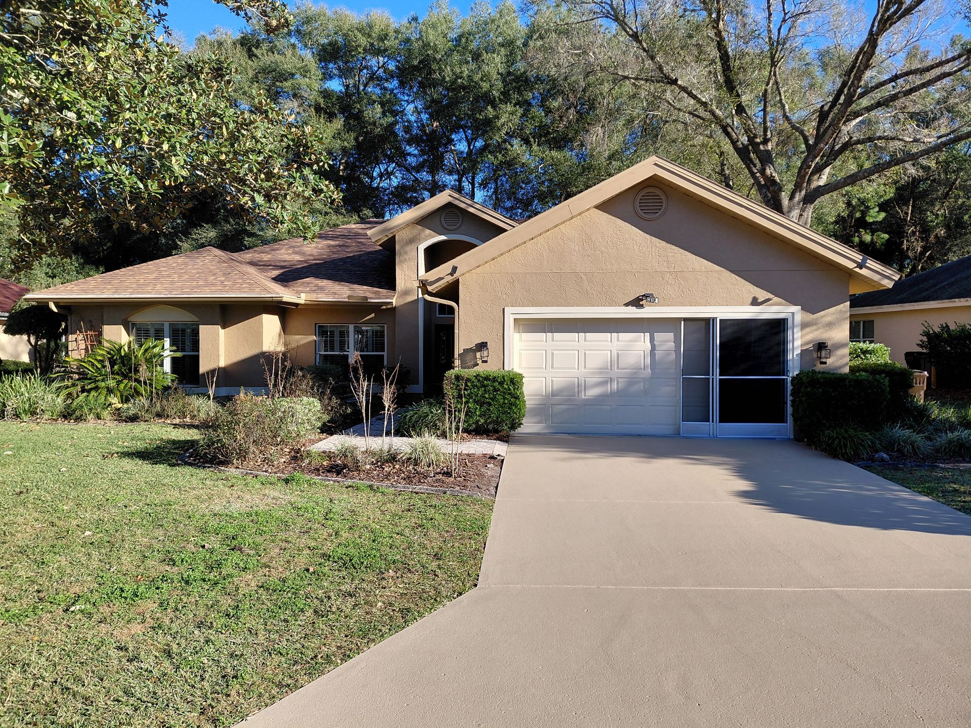 Suburban house with beige exterior, white garage, and a long driveway under trees