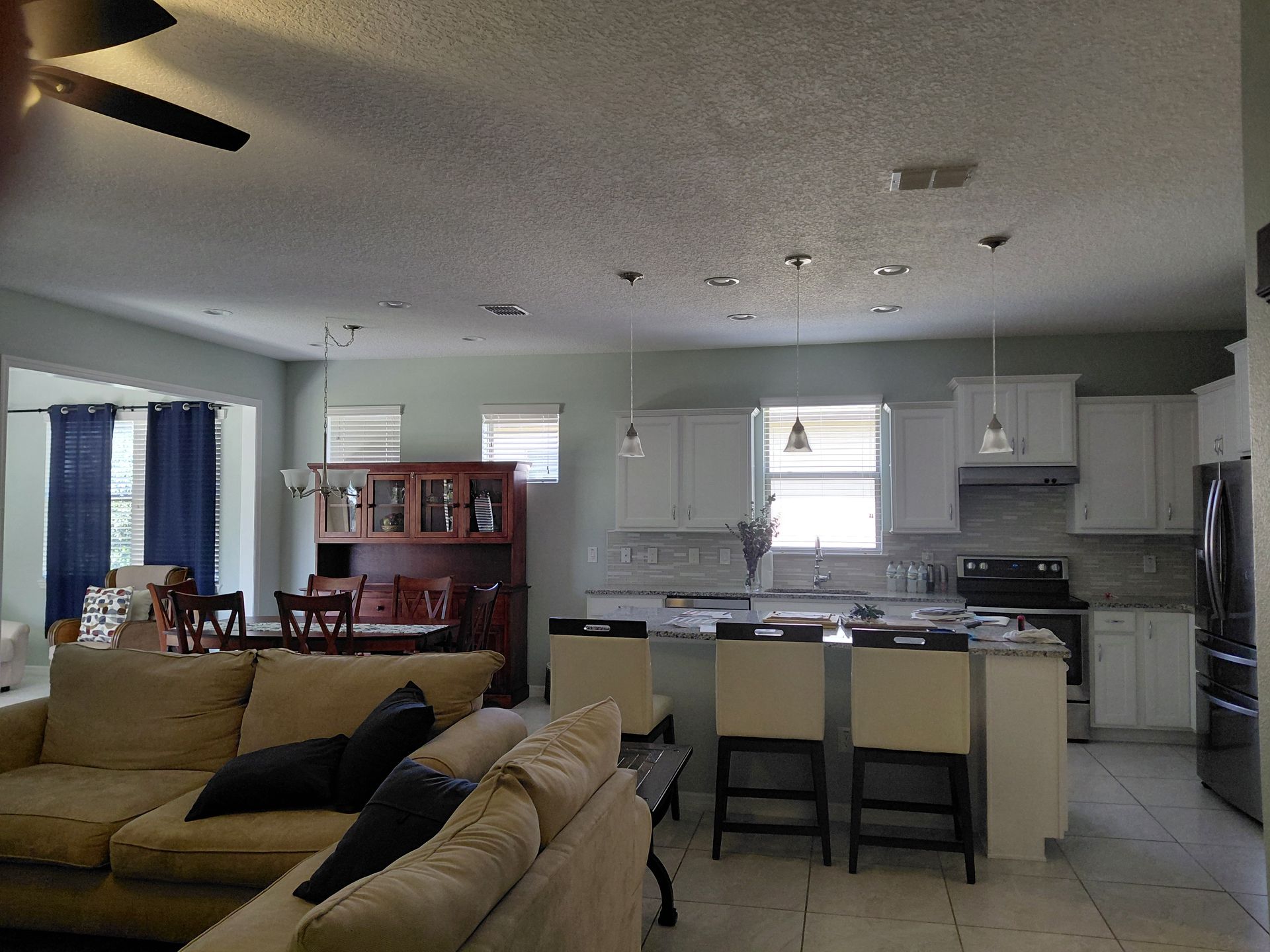 Open-plan living room and kitchen with beige couches, white cabinets, and a central island with stools.