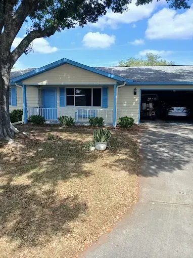 Beige house with blue trim, garage, and a tree in front, sunny day.