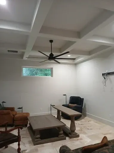 Living room with coffered ceiling, ceiling fan, window, furniture, and light-colored walls.