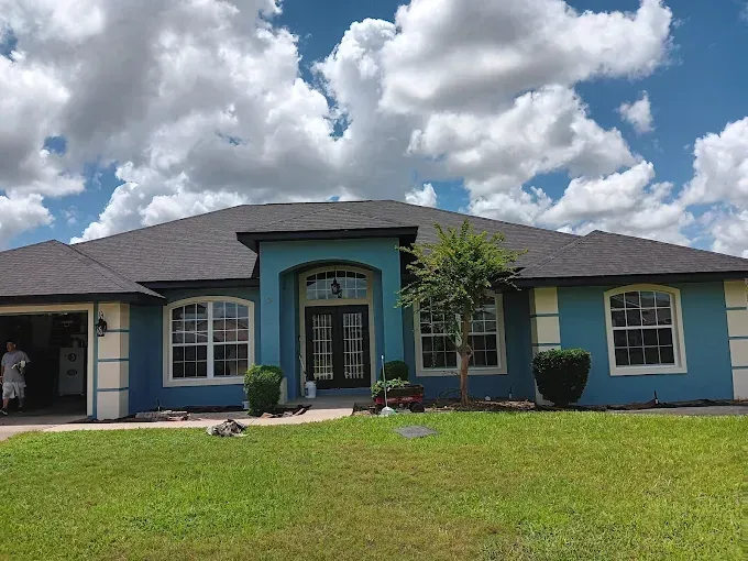 Blue house with black roof and white trim under a cloudy sky.