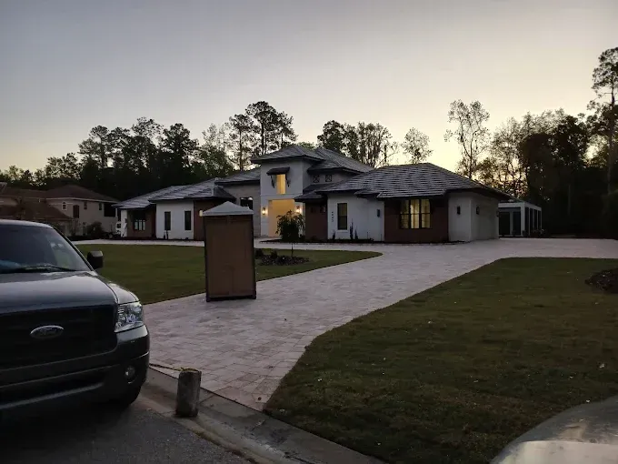 A large, modern house with a long, paved driveway and a parked truck in the foreground.