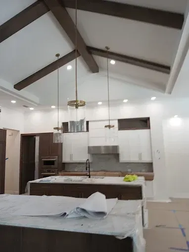 Kitchen with white cabinets, dark island, gold pendant lights, and exposed wooden beams on a vaulted ceiling.