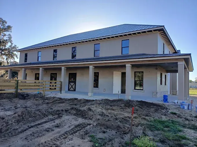 Two-story house under construction with a large front porch and metal roof.