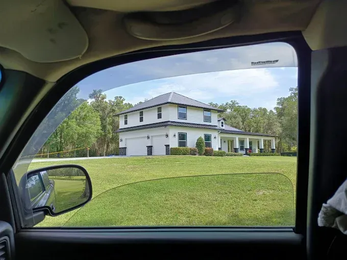 View from a car window of a large, white house with a green lawn.