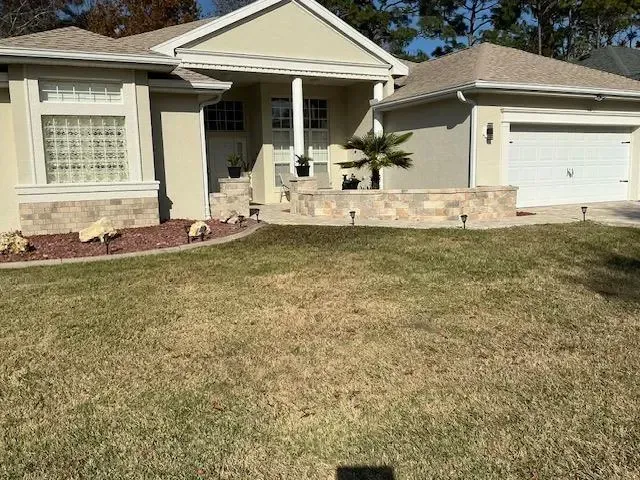 Beige stucco house with a two-car garage, front yard with brown grass, and stone-faced planter.