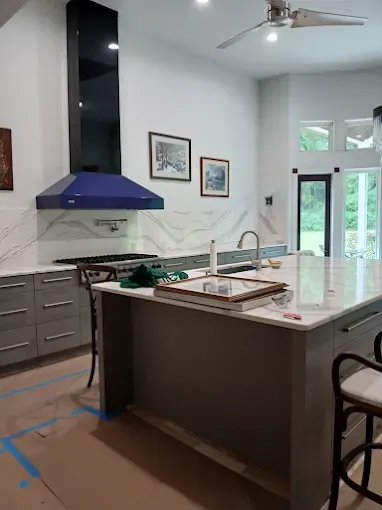 Modern kitchen with gray cabinets, marble countertops, blue range hood, and island.