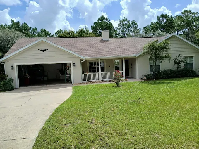 Beige house with a garage and green lawn under a partly cloudy sky.