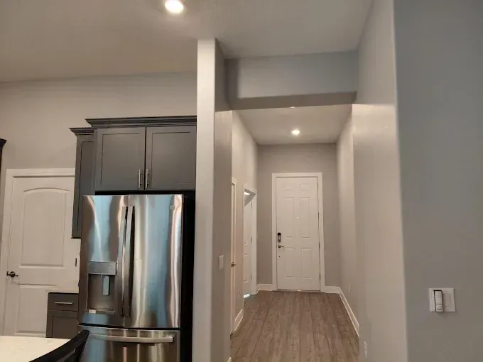 Gray kitchen with stainless steel refrigerator and hallway with a white door.