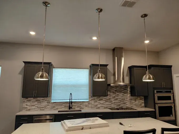 Kitchen with gray cabinets, three pendant lights, stainless steel appliances, and a mosaic backsplash.