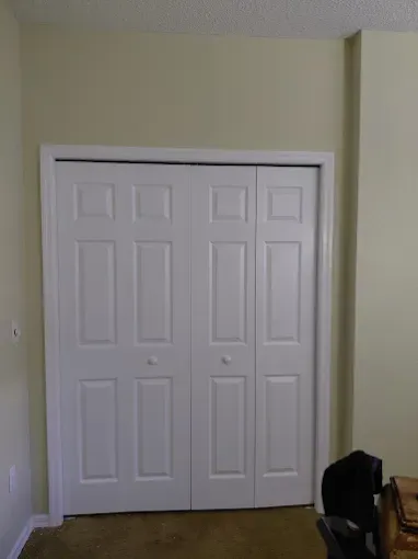 White bi-fold closet doors in a room with beige walls and a tan carpet.