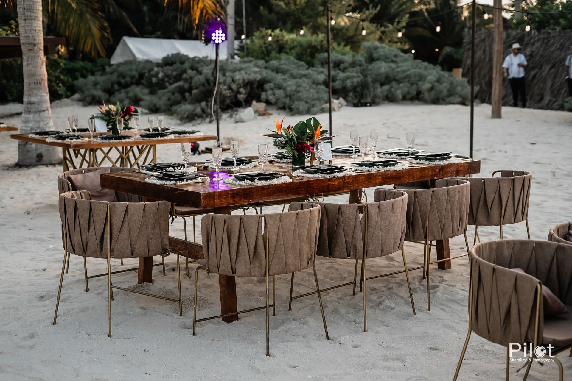 Una larga mesa de madera con sillas en una playa de arena.