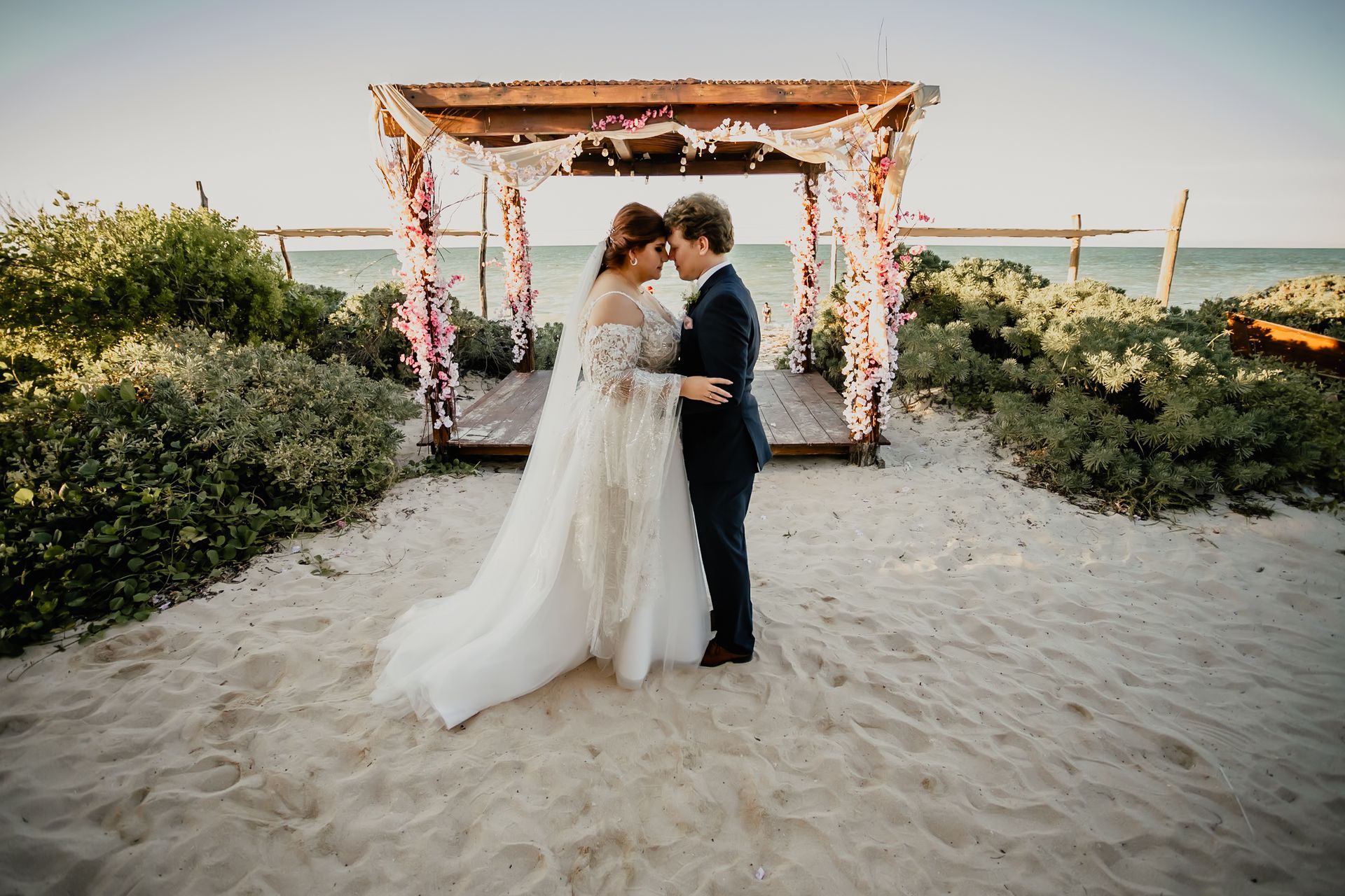 Una novia y un novio están de pie bajo un dosel en la playa.