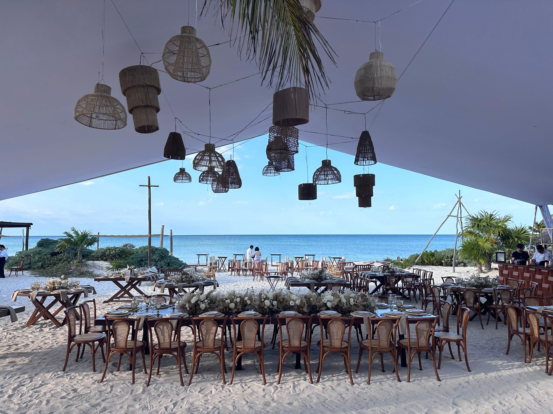 Una mesa larga y sillas están instaladas debajo de una carpa en la playa.
