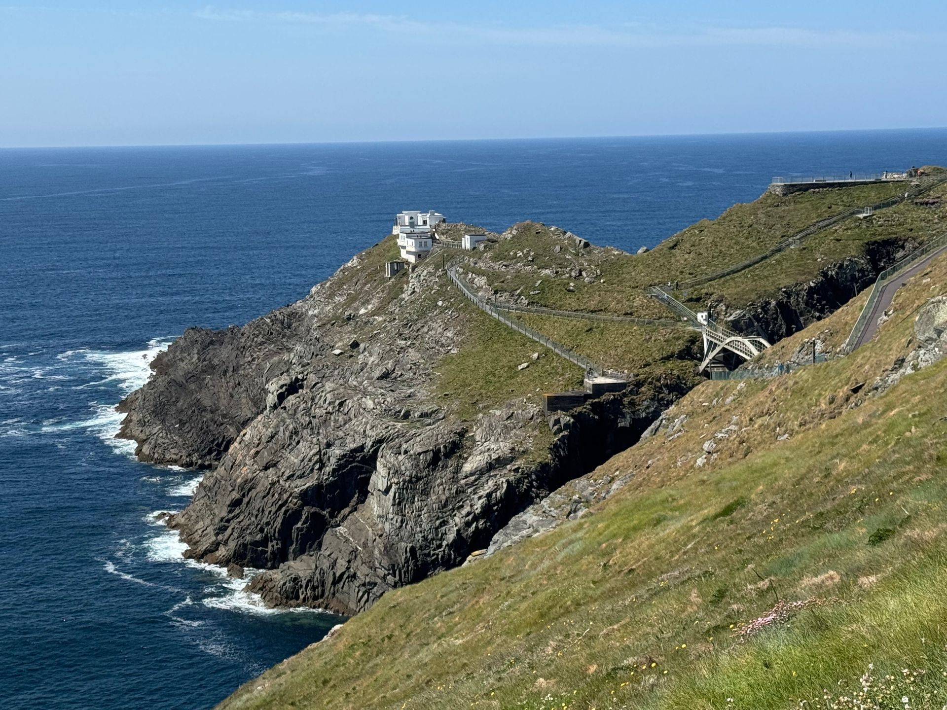 Rocky coastal headland with a lighthouse and bridge, blue sea and sky.