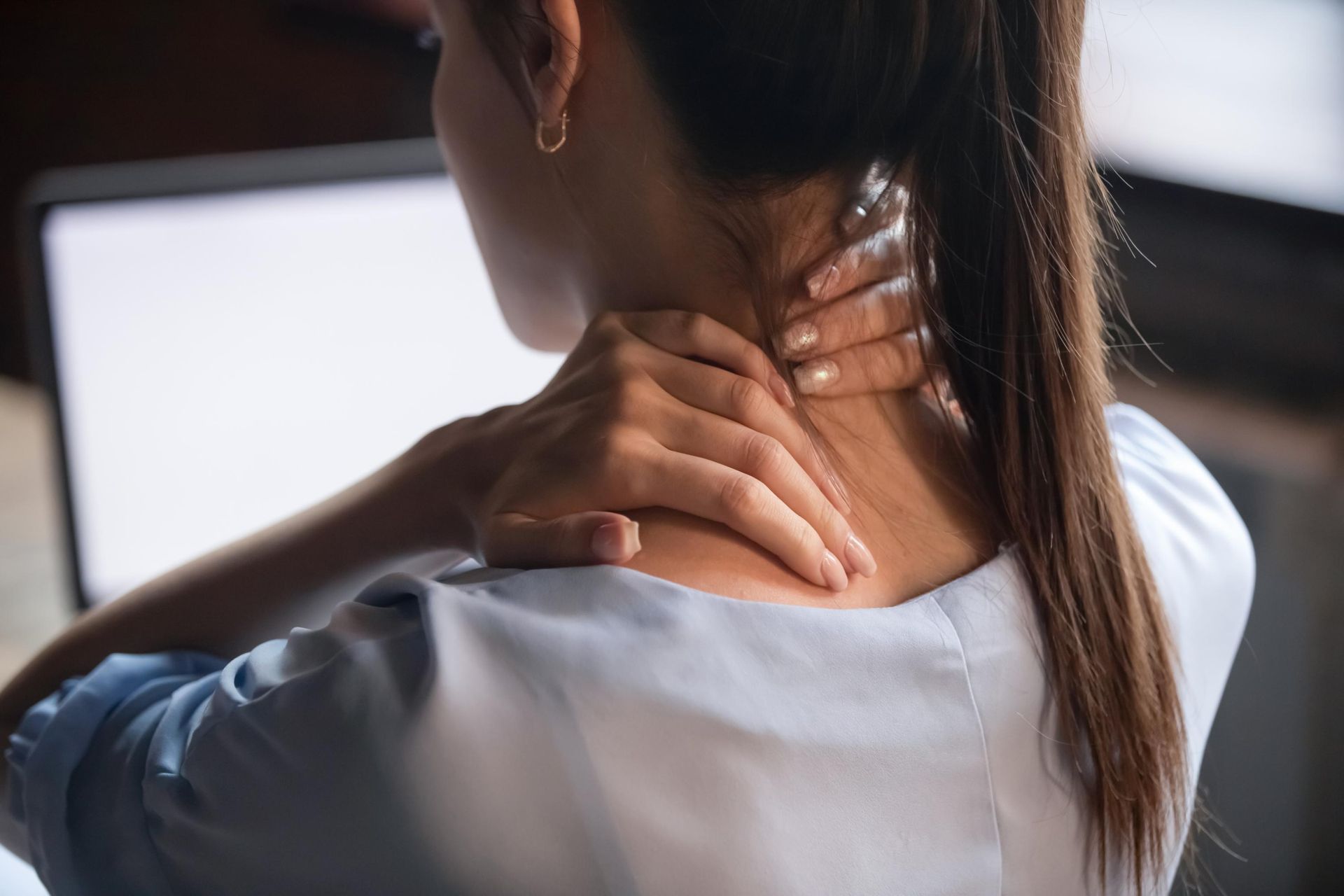 Person rubbing the back of their neck while sitting at a laptop, suggesting neck pain or strain