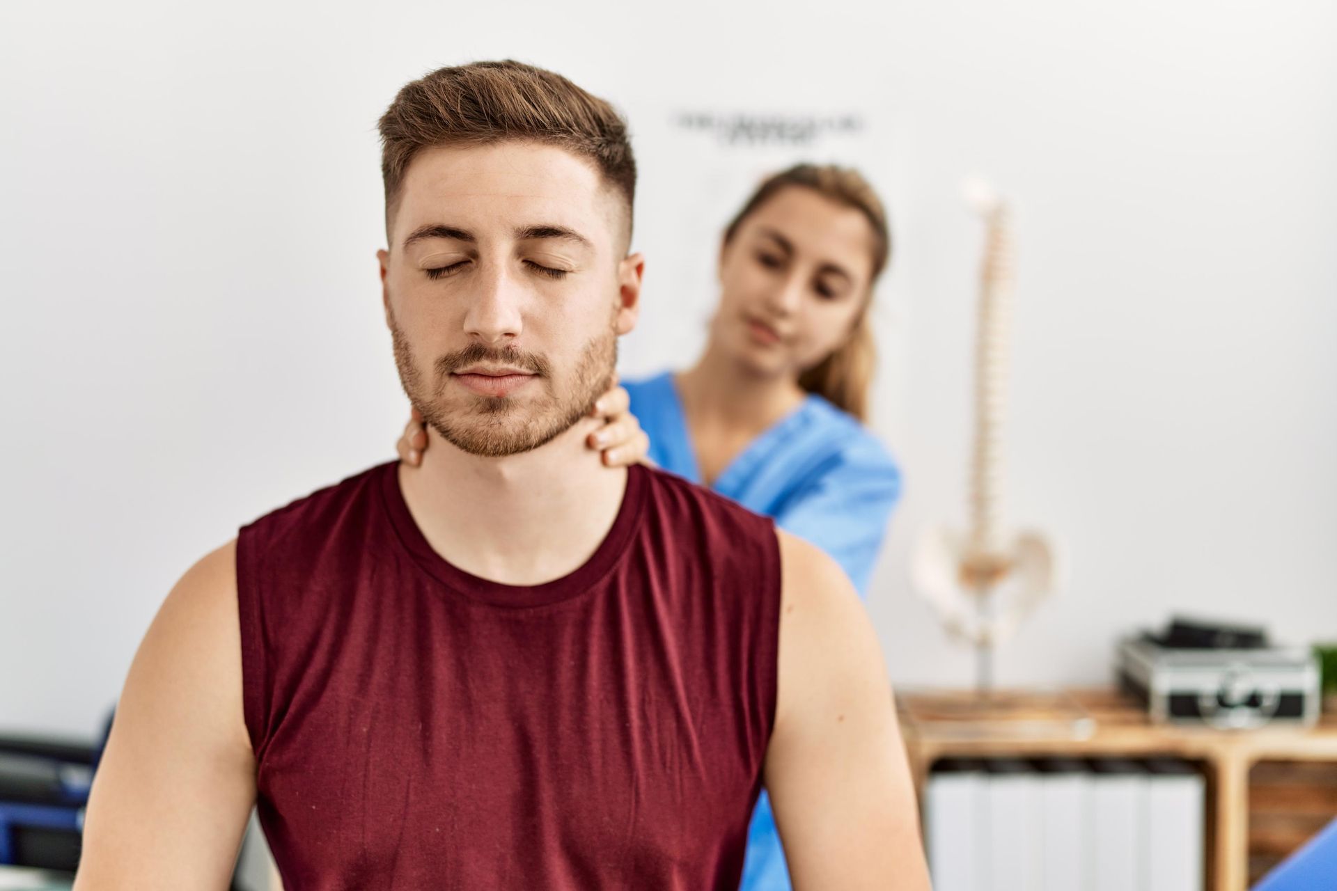 Therapist massages a man’s neck while he sits calmly with eyes closed in a bright treatment room